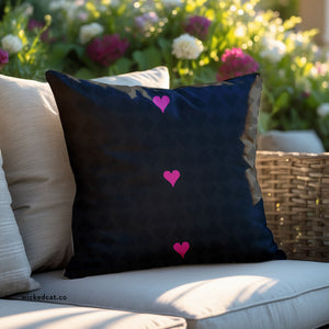 Black pillow with pink hearts on a beige couch outdoors