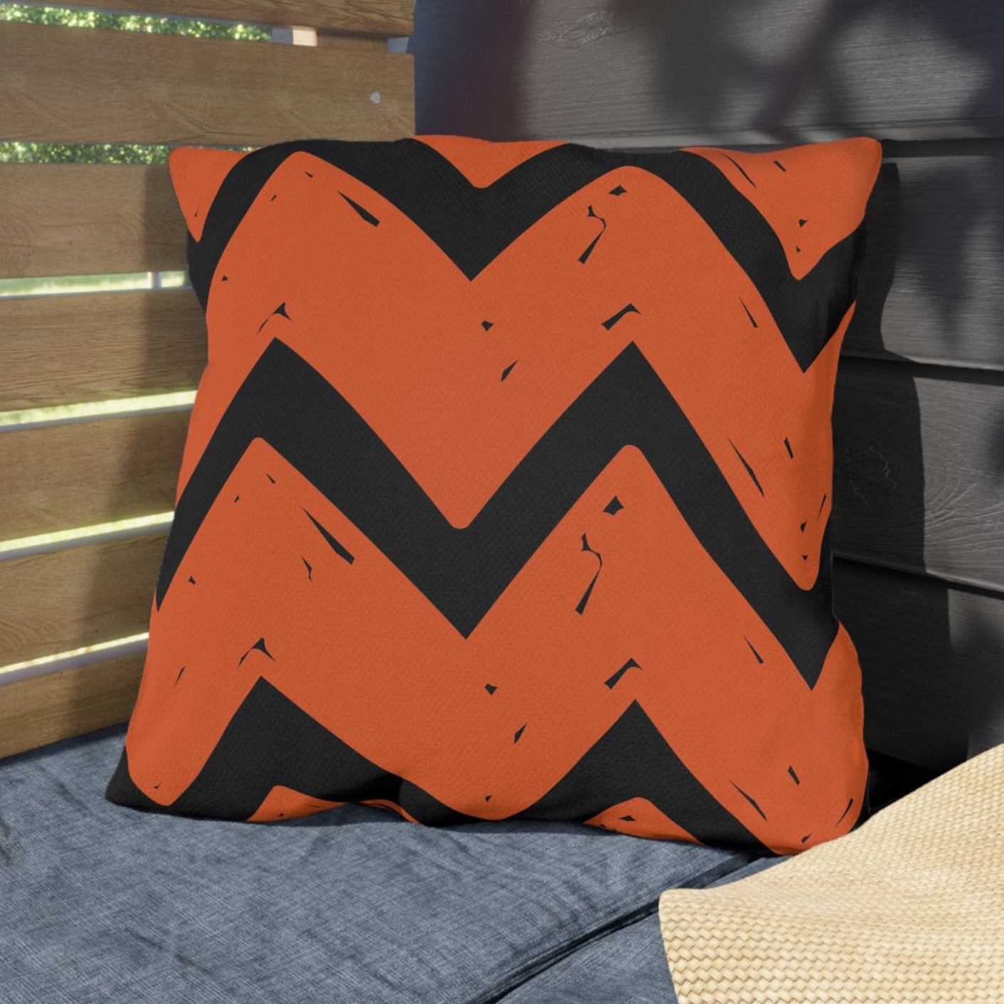 Orange and black zigzag patterned pillow on a gray cushion with a straw hat nearby.