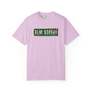 A light purple short-sleeve crewneck t-shirt featuring a distressed green 'ELM STREET' sign graphic on the chest, displayed against a solid white background.