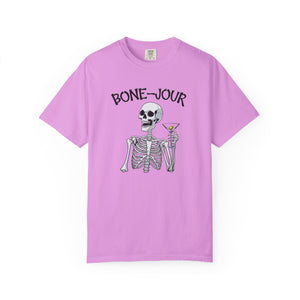 Pink t-shirt with a graphic of a skeleton holding a martini with Bone-Jour in bone style lettering at the top.
