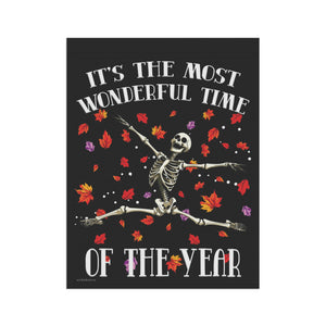 A rectangular black print or poster featuring a white skeleton sitting among scattered red, orange, yellow, and purple autumn leaves. Large white text reads “IT’S THE MOST WONDERFUL TIME OF THE YEAR” on a black background.