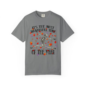 A gray short-sleeve crewneck t-shirt featuring a Halloween graphic of a dancing skeleton surrounded by red and orange autumn leaves, with the text 'IT'S THE MOST WONDERFUL TIME OF THE YEAR'.