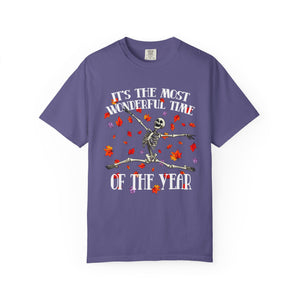 A purple short-sleeve crewneck t-shirt featuring a Halloween graphic of a dancing skeleton surrounded by red and orange leaves, with the text 'IT'S THE MOST WONDERFUL TIME OF THE YEAR'.