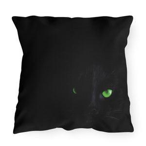 A square black throw pillow featuring a printed design of a black cat's face with glowing green eyes, shown against a plain white background.