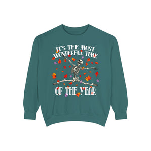 A teal crewneck sweatshirt featuring a Halloween graphic of a dancing skeleton surrounded by colorful autumn leaves, with the text 'IT'S THE MOST WONDERFUL TIME OF THE YEAR'.