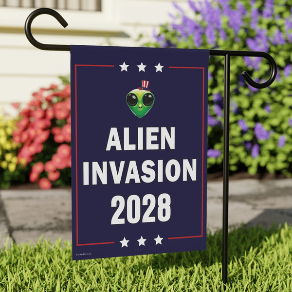 Garden flag with 'Alien Invasion 2028' design on a grassy lawn with flowers in the background