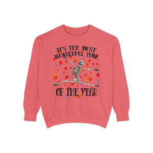 A coral pink crewneck sweatshirt featuring a Halloween graphic of a dancing skeleton surrounded by falling autumn leaves, with the text 'IT'S THE MOST WONDERFUL TIME OF THE YEAR'.