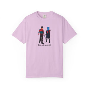 Pink t-shirt with graphic design of two characters and text 'Tis' only a scratch on a white background