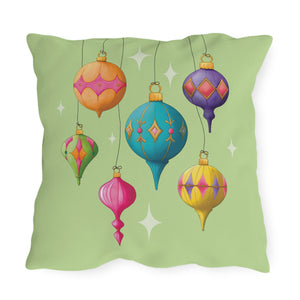 A square throw pillow featuring a colorful illustration of hanging Christmas ornaments on a light green background.