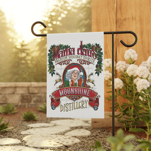 Decorative garden flag with 'Mama Claus Moonshine Distillery' design on a stand outdoors.