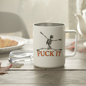 White mug with skeleton design and 'F*** IT' text on a table with a teapot and bread in the background.