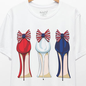White t-shirt with red white and blue high-heeled shoes design on a hanger against a white background.