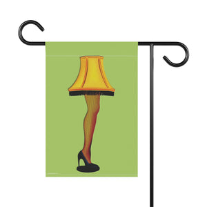 A rectangular garden flag hanging from a black metal stand against a white background. The flag features an illustration of the 'This is fine' lamp from A Christmas Story, with a yellow fringed lampshade, fishnet stocking leg, and black high heel on a light green background.