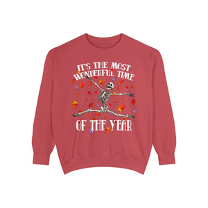 A dusty red crewneck sweatshirt featuring a Halloween graphic of a dancing skeleton surrounded by falling autumn leaves, with the text 'IT'S THE MOST WONDERFUL TIME OF THE YEAR'.