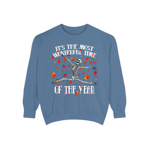 A dusty blue crewneck sweatshirt featuring a Halloween graphic of a dancing skeleton surrounded by falling autumn leaves, with the text 'IT'S THE MOST WONDERFUL TIME OF THE YEAR'.