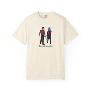 Beige t-shirt with graphic design of two characters and text 'Tis' only a scratch on a white background