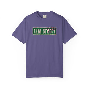 A purple short-sleeve crewneck t-shirt featuring a distressed green 'ELM STREET' sign graphic on the chest, displayed against a plain white background.