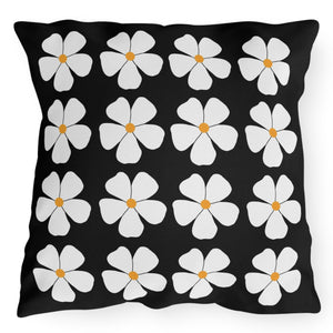 A square-shaped accent pillow with a black background and a white floral pattern consisting of flowers with yellow centers.