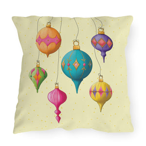 A square decorative throw pillow featuring a colorful illustration of hanging Christmas ornaments on a pale yellow background with small gold dots.