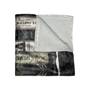 A folded throw blanket featuring a black and white gothic horror-themed print with text and illustrations from Michael Myers' 'Exorcism' and 'HALLOWEEN', with a soft light gray fleece backing visible on the reverse side.