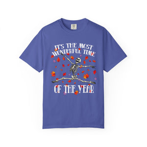 A royal blue short-sleeve t-shirt with a Halloween-themed graphic on the front. The graphic features a skeleton sitting on a log with red and orange autumn leaves, accompanied by the text 'IT'S THE MOST WONDERFUL TIME OF THE YEAR'.