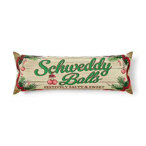 A rectangular decorative pillow featuring a rustic wood-plank design with the words 'Schweddy Balls' in green script, smaller text reading 'Festively Salty & Sweet,' and holiday-themed illustrations including pine branches, red berries, and ornaments.