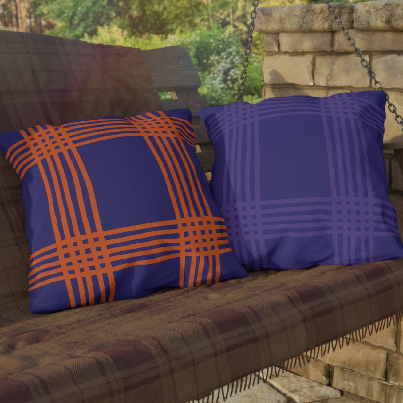 Brown swing with blue and orange pillows against a stone wall and greenery background