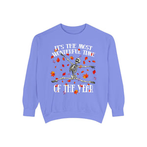 A light periwinkle blue crewneck sweatshirt featuring a festive graphic of a dancing skeleton surrounded by red and orange autumn leaves, with the text 'IT'S THE MOST WONDERFUL TIME OF THE YEAR' in white.