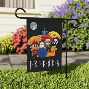 A rectangular garden flag displayed on a black metal stand in a grassy yard. The flag has a black background with a colorful illustration of horror movie characters sitting on a couch under yellow and red umbrellas, plus the word 'F.