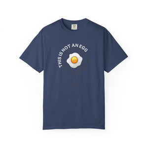 A navy blue short-sleeve t-shirt with a graphic of a fried egg inside a pan outline, with the text 'THIS IS NOT AN EGG' arched above it, displayed on a clean white background.