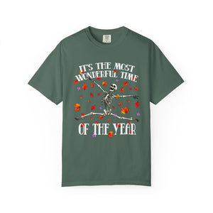 A dark green short-sleeve t-shirt with a Halloween graphic of a dancing skeleton surrounded by red and orange autumn leaves, with the text 'IT'S THE MOST WONDERFUL TIME OF THE YEAR'.