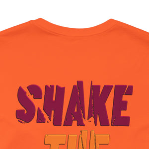 Close-up of an orange t-shirt featuring a distressed dark magenta graphic that reads 'SHAKE' partially visible below in orange.