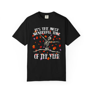 A black short-sleeve crewneck t-shirt featuring a Halloween graphic of a skeleton dancing amidst orange and purple autumn leaves, with the text 'IT'S THE MOST WONDERFUL TIME OF THE YEAR' in white.
