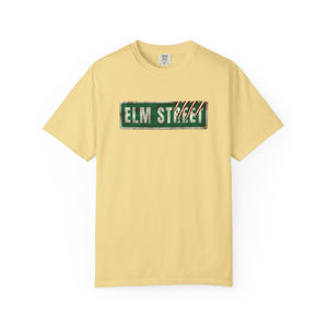 A pale yellow short-sleeve crewneck t-shirt featuring a distressed green 'ELM STREET' sign graphic printed across the chest.