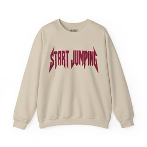 A beige crewneck sweatshirt featuring the phrase 'START JUMPING' printed across the chest in a stylized, jagged dark red font, displayed on a clean white background.