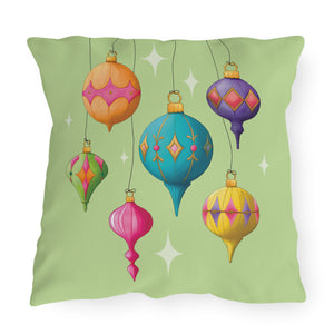A square throw pillow featuring a retro-style illustration of six colorful hanging Christmas ornaments on a light green background with white star accents.
