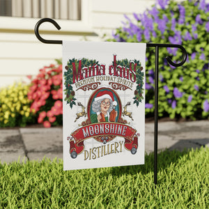 Garden flag with 'Mama Claus Moonshine Distillery' design on grass with flowers in the background