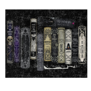 A decorative throw blanket featuring a row of gothic-style illustrated book spines on a dark textured background, with the title 'Love Potion No.' and the name 'Witchy Chris' visible on the artwork.