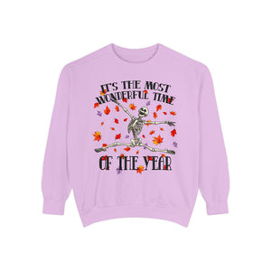 A light purple crewneck sweatshirt featuring a festive graphic of a skeleton dancing amidst red and orange autumn leaves, with the text 'IT'S THE MOST WONDERFUL TIME OF THE YEAR'.