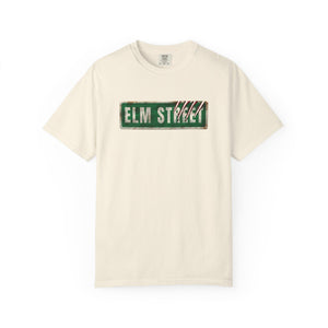An off-white crewneck t-shirt featuring a distressed green 'ELM STREET' sign graphic printed across the chest.