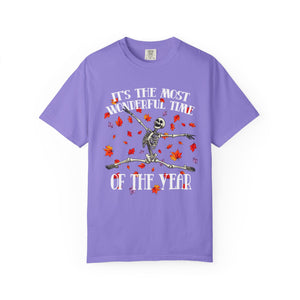 A purple short-sleeve crewneck t-shirt featuring a graphic of a dancing skeleton surrounded by red autumn leaves, with the text 'IT'S THE MOST WONDERFUL TIME OF THE YEAR' in white.