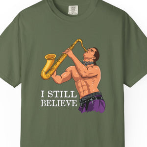 Green t-shirt with a graphic of a man playing a saxophone and text 'I STILL BELIEVE' on a white background. 80s Pop Culture The Lost Boys Shirt.