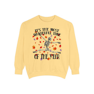 A pale yellow crewneck sweatshirt featuring a Halloween graphic of a skeleton dancing amidst red and orange autumn leaves, with the text 'IT'S THE MOST WONDERFUL TIME OF THE YEAR'.
