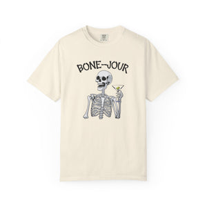 Ivory t-shirt with a graphic of a skeleton holding a martini with Bone-Jour in bone style lettering at the top.