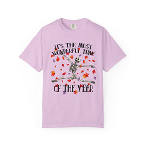 A light purple short-sleeve t-shirt with a graphic of a skeleton dancing amidst red and orange autumn leaves, with the text 'IT'S THE MOST WONDERFUL TIME OF THE YEAR' printed around it.