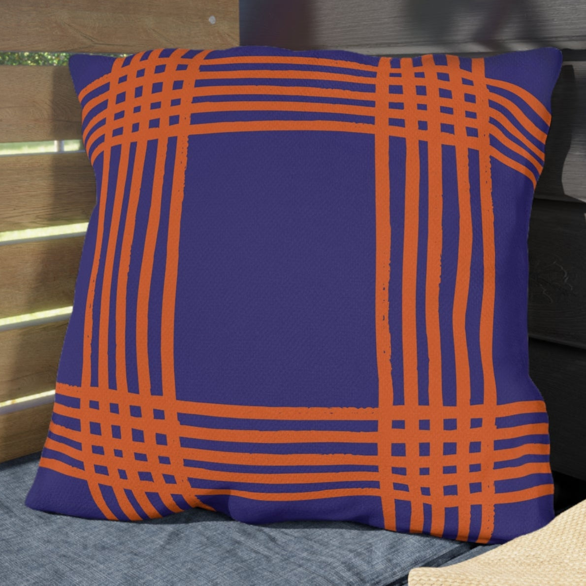 Blue pillow with orange lines on a gray cushion next to a straw hat against a wooden and dark panel background.