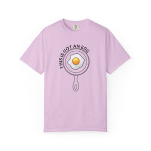 A light purple short-sleeve t-shirt with a graphic of a frying pan containing a fried egg, with the text 'THIS IS NOT AN EGG' arched above it, displayed on a clean white background.