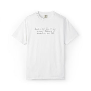 A white short-sleeve crewneck t-shirt with a small black printed quote on the chest reading 'Rain is just God crying, probably because of something you did.'.