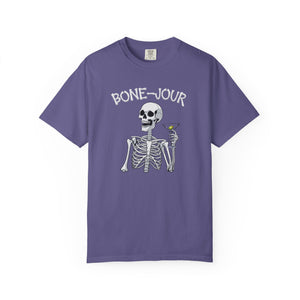 Purple t-shirt with a graphic of a skeleton holding a martini with Bone-Jour in bone style lettering at the top.