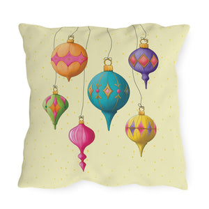 A square decorative throw pillow featuring a colorful illustration of hanging Christmas ornaments on a pale yellow background with small gold dots.